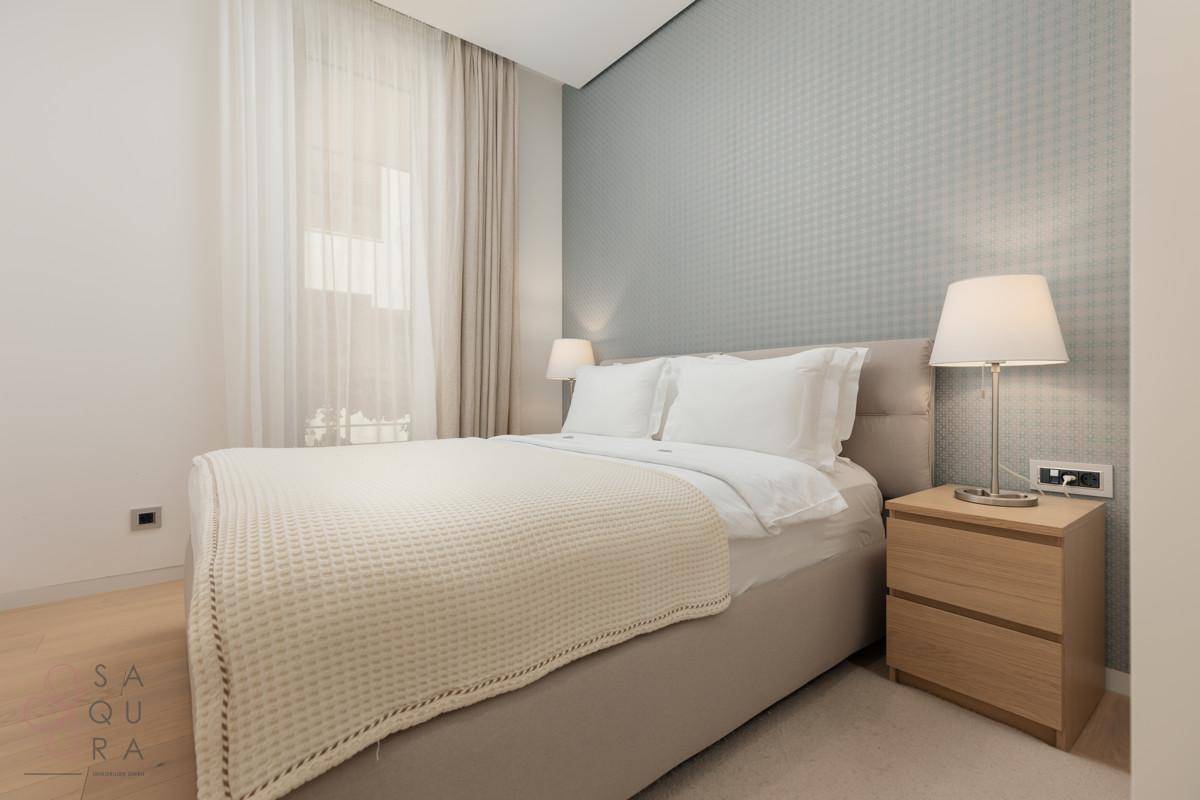 Ein helles Schlafzimmer mit Doppelbett, Nachttischen und einer dezent gemusterten Wand, modern eingerichtet.