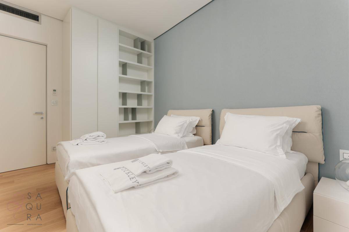 Helles Schlafzimmer mit zwei Einzelbetten, Einbauregalen und Holzboden in modernem Design.