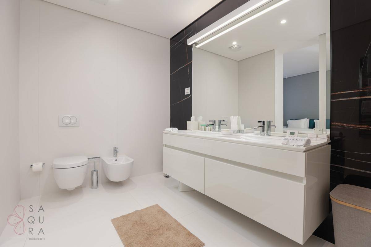 Stilvolles Badezimmer mit Doppelwaschbecken, Bidet und einer eleganten schwarzen Marmorwand als Akzent.