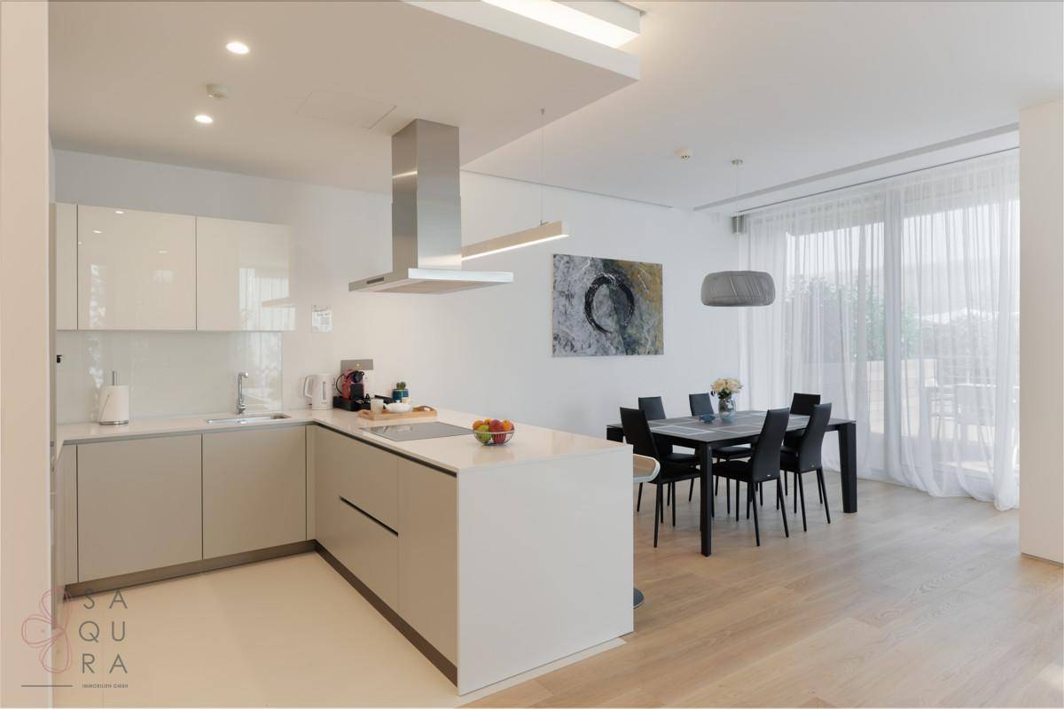 Moderne offene Küche mit heller Einrichtung und Essbereich, daneben große Fenster mit Vorhängen.