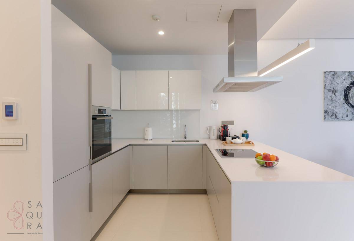 Elegante, moderne Küche mit weißen Hochglanzfronten, integrierten Geräten und heller Arbeitsplatte.