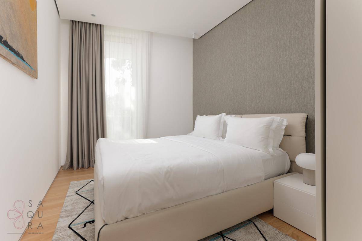 Helles Schlafzimmer mit Doppelbett, Holzboden und einem Fenster mit Vorhängen, modern eingerichtet.