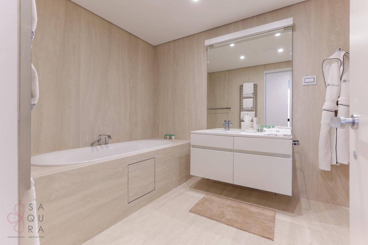 Modernes Badezimmer mit integrierter Badewanne, schwebendem Waschtisch und beigefarbenen Fliesen.