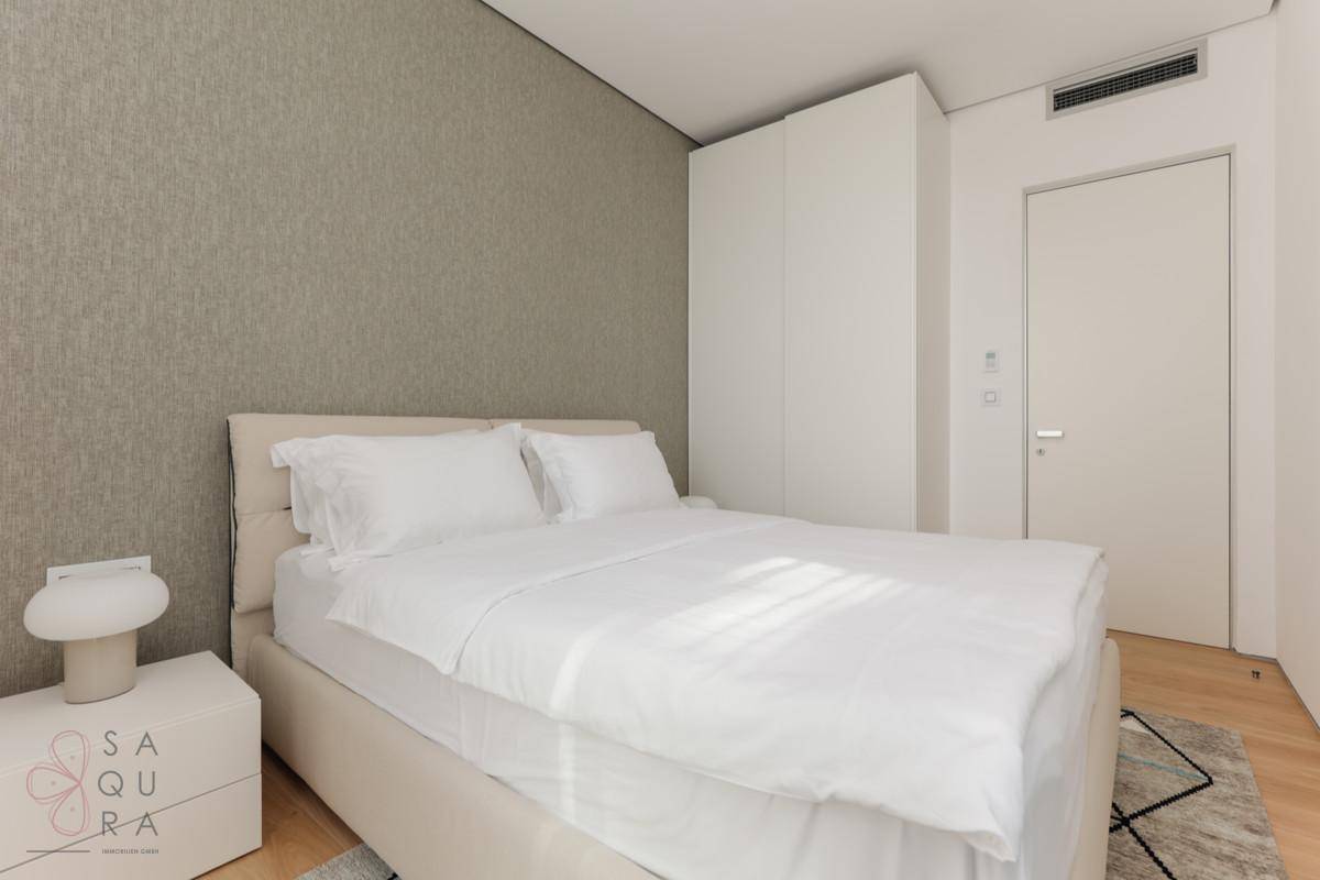 Gemütliches Schlafzimmer mit Doppelbett, Holzboden und einer strukturierten Wandtapete in neutralen Tönen.