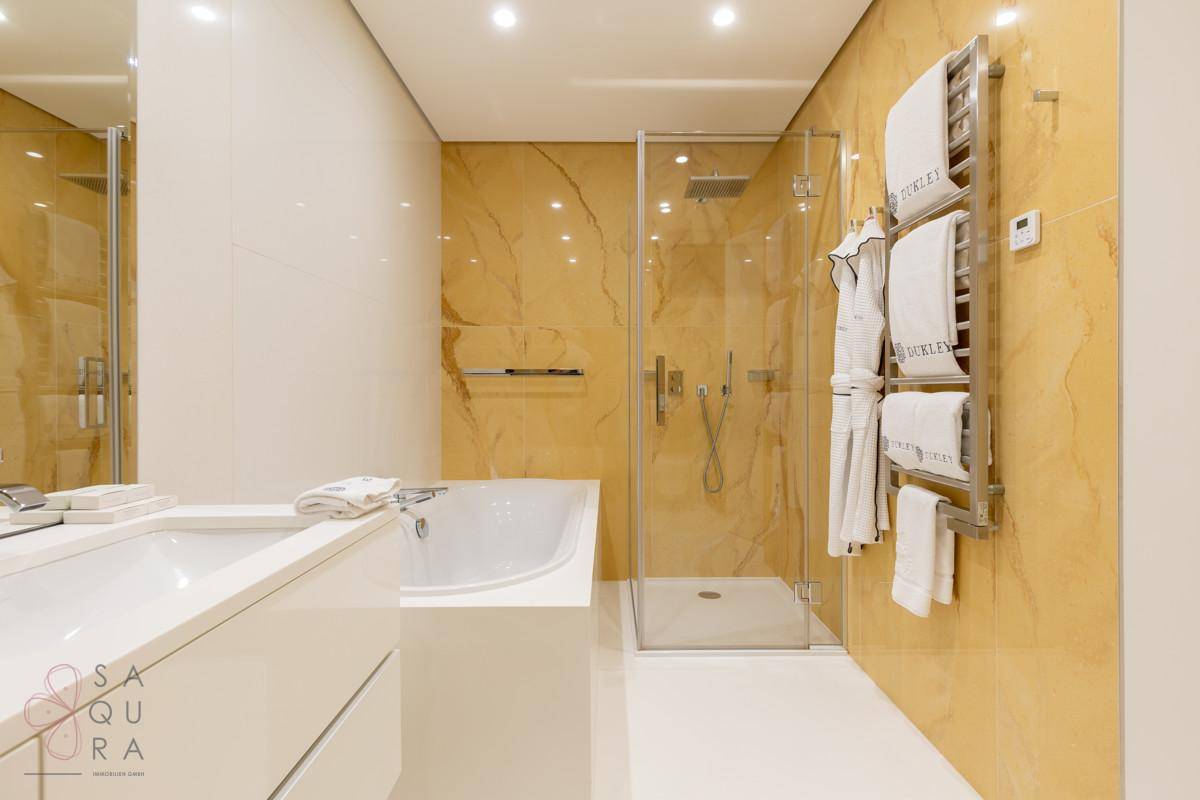 Elegantes Badezimmer mit Badewanne, begehbarer Dusche und beheiztem Handtuchhalter in warmen Farbtönen und Fliesen.