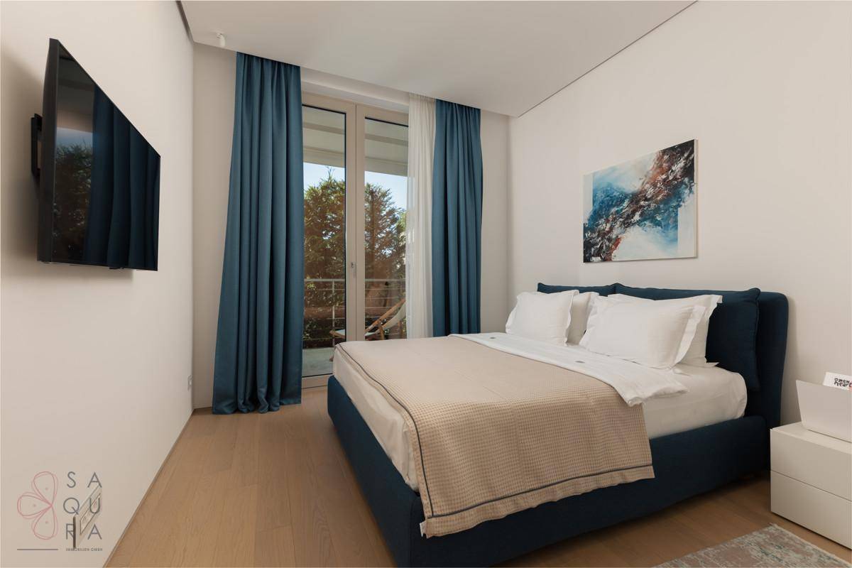 Gemütliches Schlafzimmer mit blauem Bett, Wandfernseher und Zugang zum Balkon.