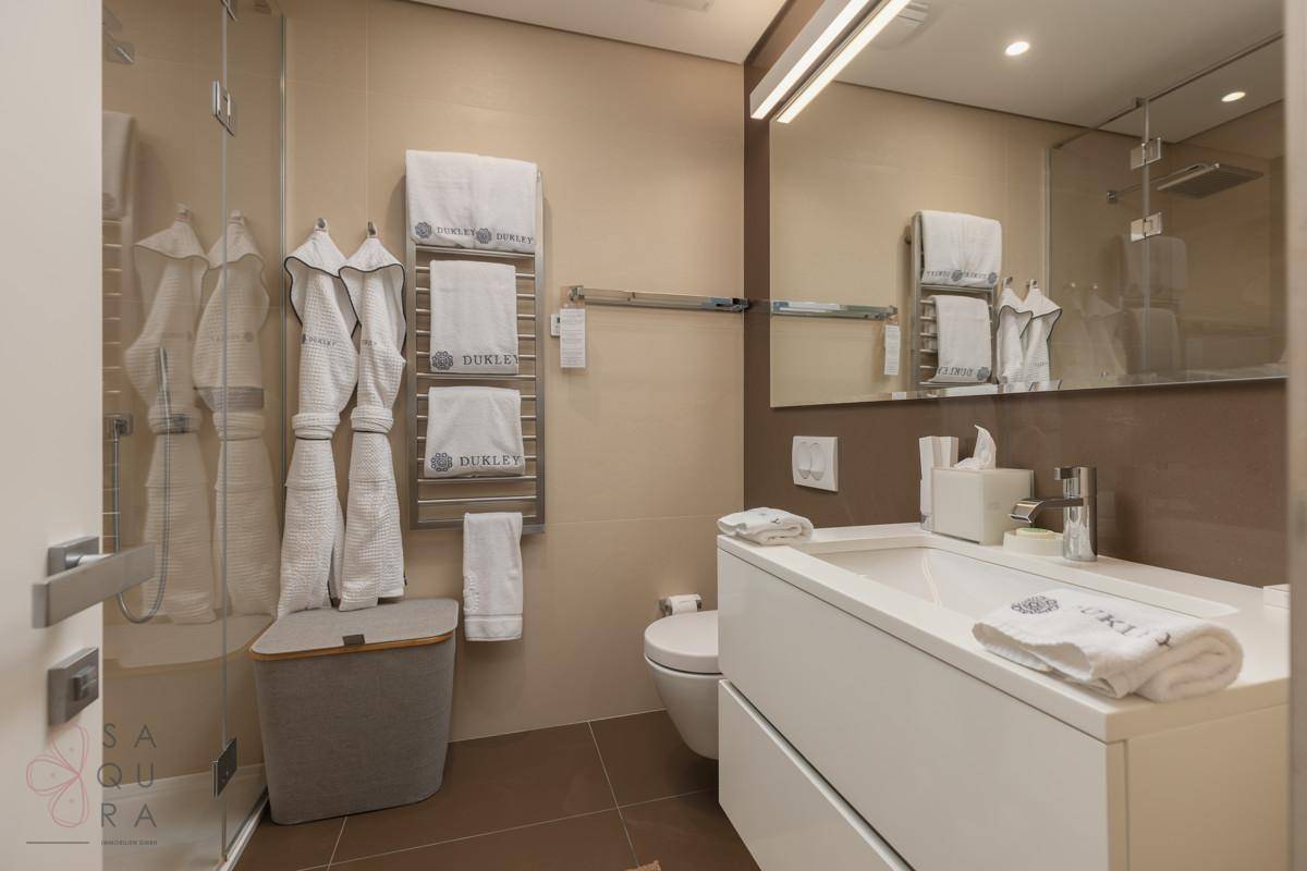 Modernes Badezimmer mit begehbarer Dusche, Einzelwaschbecken und beheiztem Handtuchhalter in neutralen Farben.