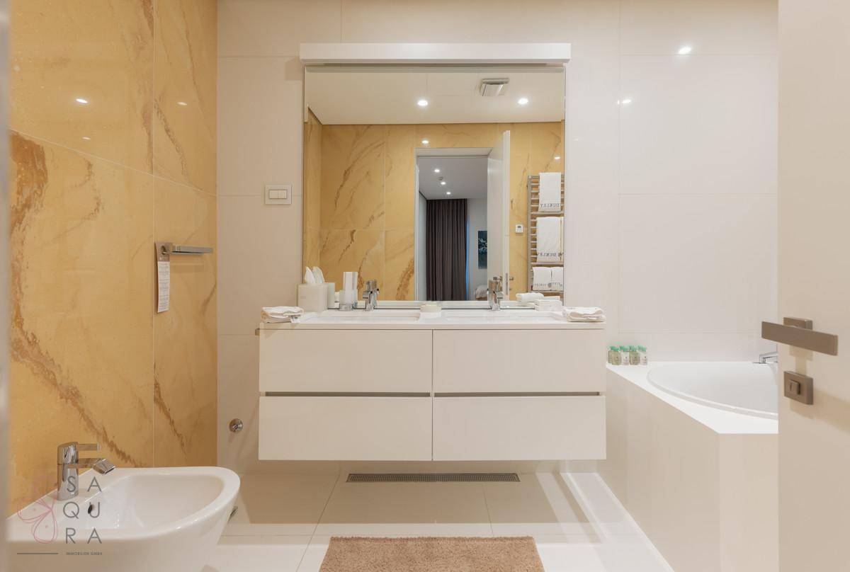 Helles Badezimmer mit Doppelwaschbecken, Badewanne und Bidet, ausgestattet mit modernen Fliesen und Spiegel.