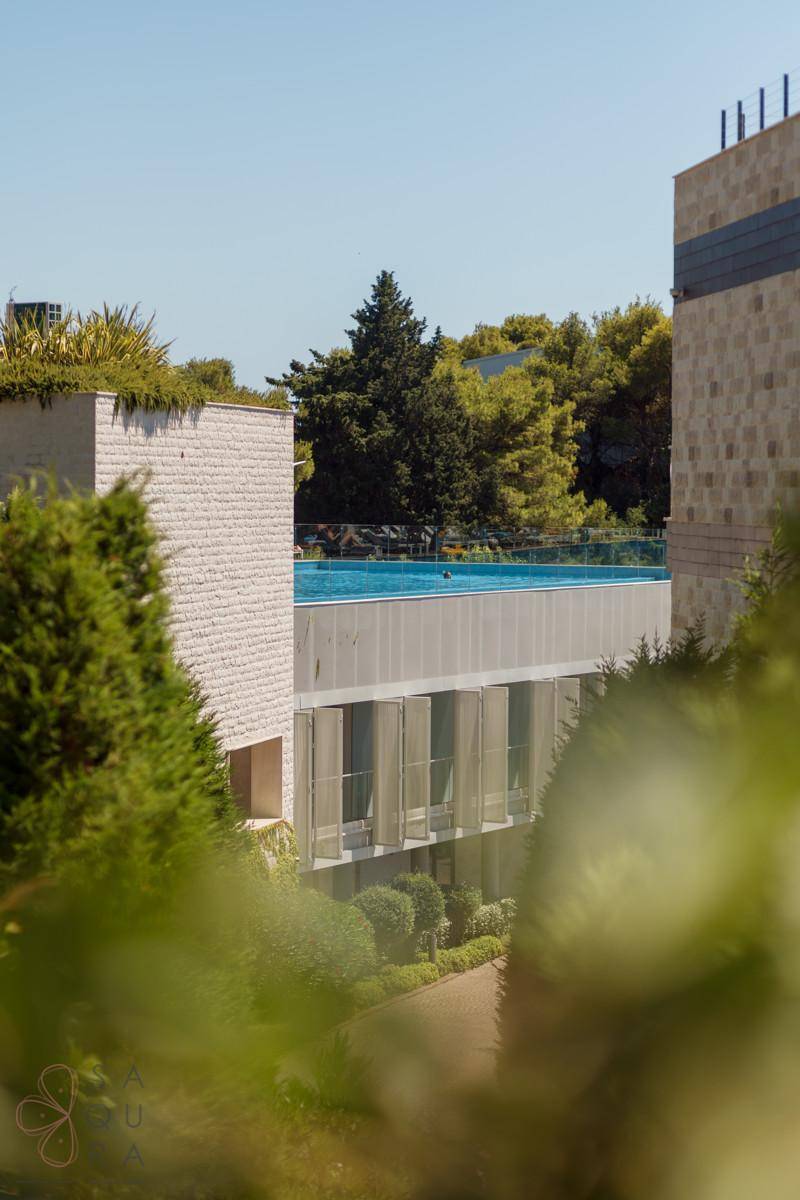 Moderne Architektur mit einem Infinity-Pool auf dem Dach, umgeben von üppiger Vegetation und Bäumen.