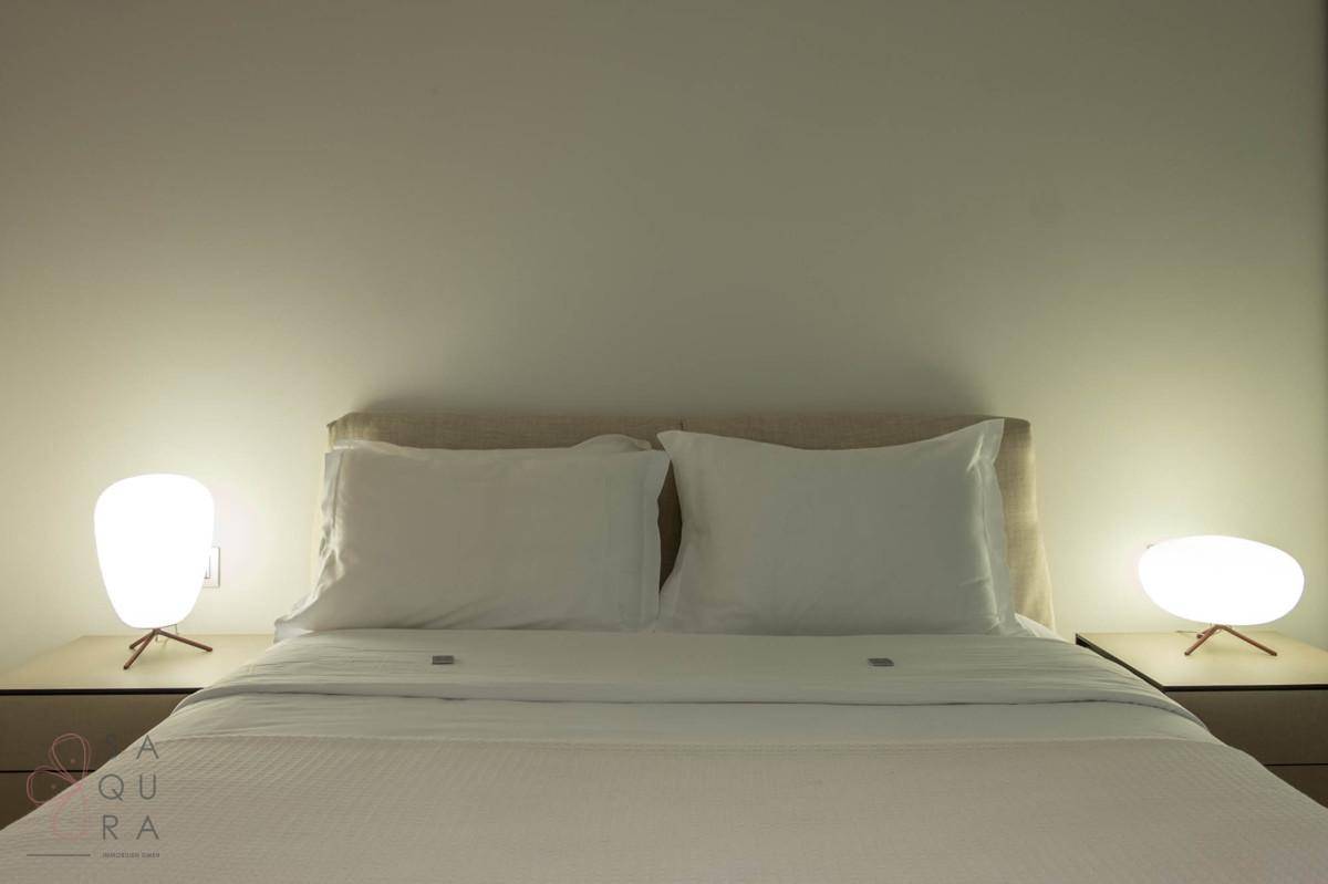Gemütliches Schlafzimmer mit einem großen Bett, weißen Laken und modernen Nachttischlampen.