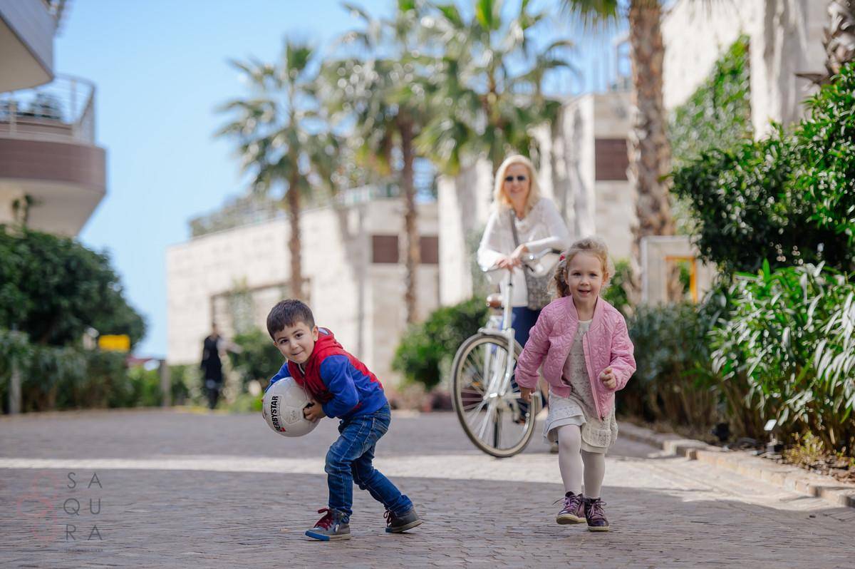 Zwei Kinder spielen fröhlich auf einem gepflasterten Weg, umgeben von Palmen und modernen Gebäuden.