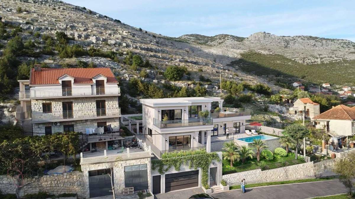 Moderne Villa eingebettet in eine bergige Landschaft mit umliegenden Gebäuden und viel Grün.