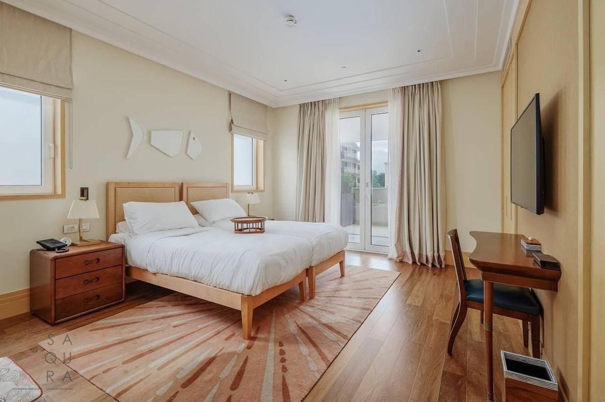 Helles Schlafzimmer mit zwei Einzelbetten, Holzboden und Zugang zu einem Balkon.