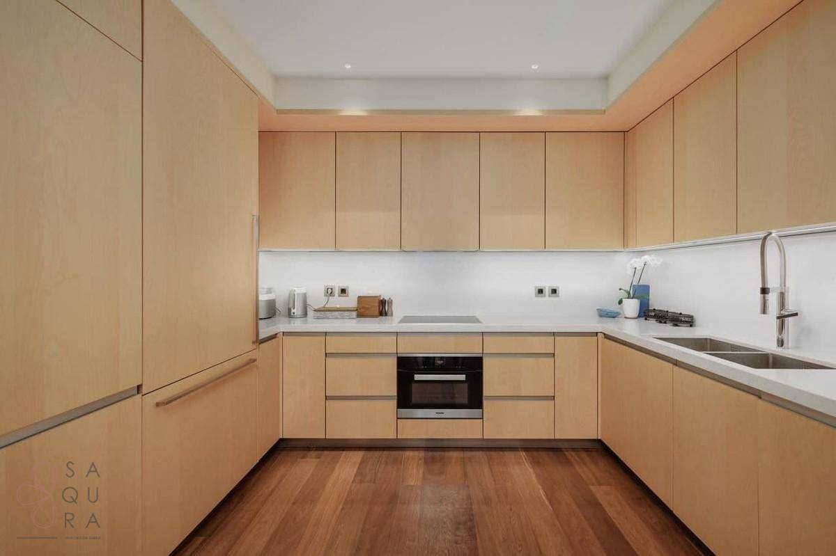Moderne Einbauküche mit hellen Holzfronten, integrierten Geräten und Holzboden.