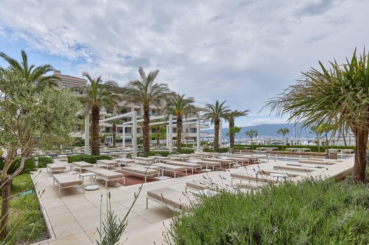Weitläufiger Poolbereich mit zahlreichen Liegestühlen, Palmen und Blick auf das Meer.
