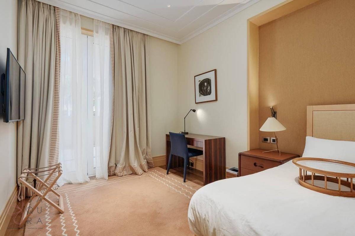 Schlafzimmer mit Schreibtisch, Fernseher und großen Fenstern, die viel Licht hereinlassen.
