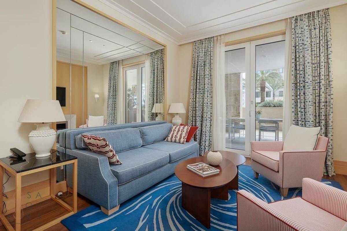 Helles Wohnzimmer mit blauem Sofa, gemustertem Teppich und Zugang zur Terrasse.