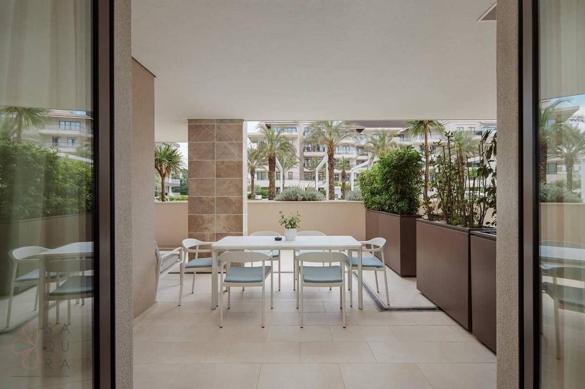 Große überdachte Terrasse mit Esstisch und Stühlen, umgeben von Pflanzen und Palmen.