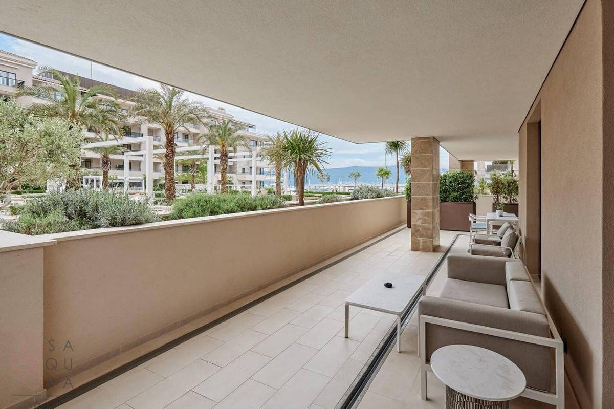 Geräumige überdachte Terrasse mit Loungemöbeln und Blick auf die Poolanlage und Palmen.