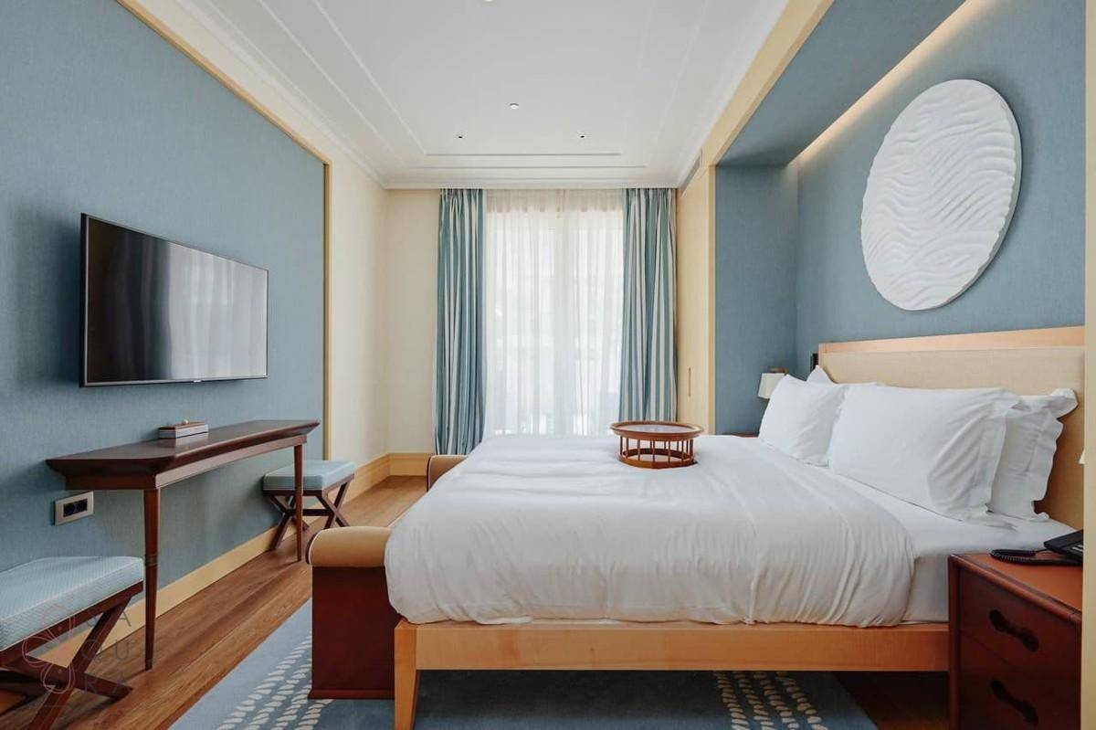 Elegantes Schlafzimmer mit großem Bett, blauer Akzentwand und Holzboden.