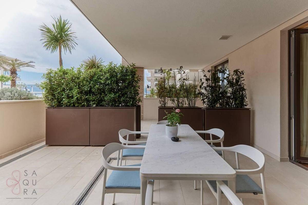 Heller Essbereich auf einer überdachten Terrasse mit großem Tisch und Pflanzenkübeln.