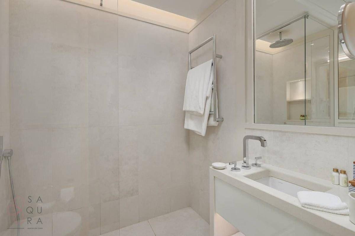 Helles Badezimmer mit großer begehbarer Dusche, modernem Waschbecken und Handtuchhalter.