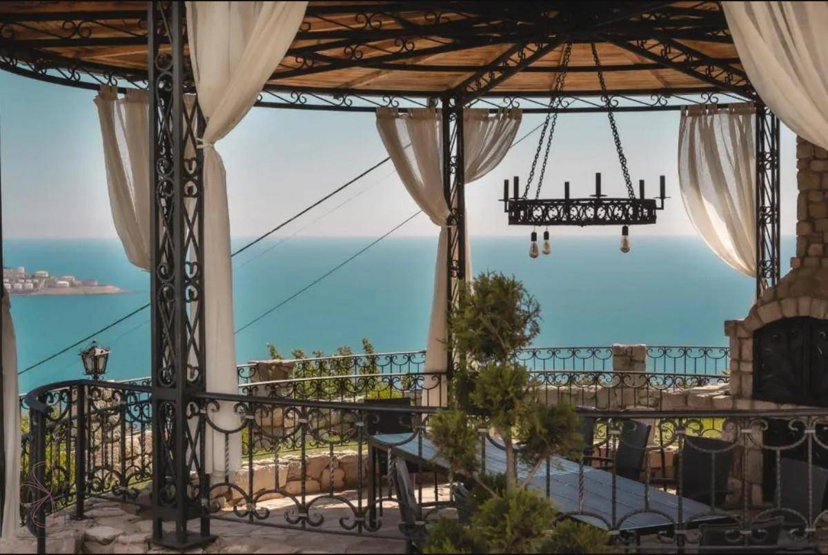 Gemütlicher Pavillon mit Esstisch und Meerblick, ausgestattet mit Vorhängen und einem dekorativen Kronleuchter.