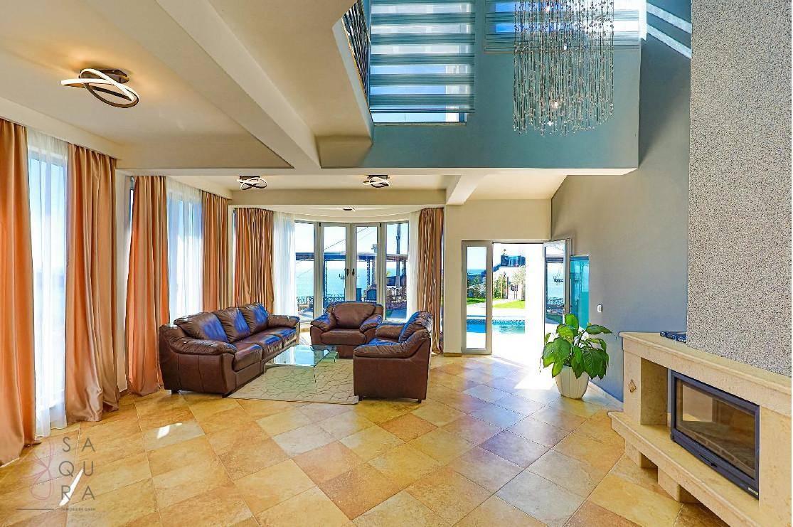 Großzügiges Wohnzimmer mit Kamin, Ledersofas und Zugang zum Poolbereich durch große Glastüren.