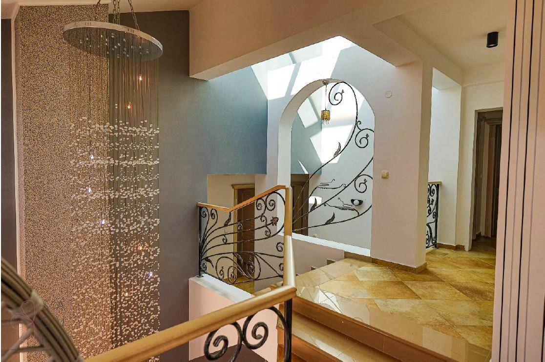 Elegante Treppe mit schmiedeeisernem Geländer und einem großen Kronleuchter, der den Flur beleuchtet.