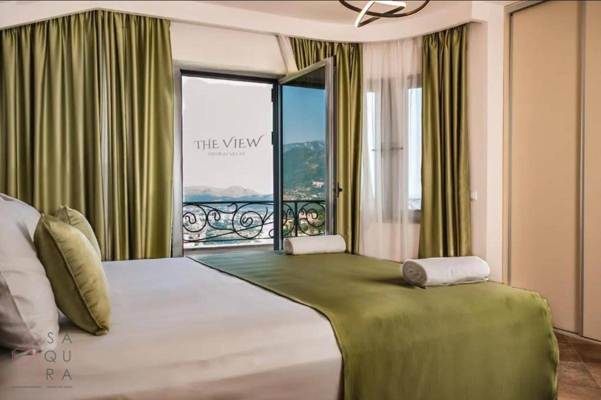 Schlafzimmer mit Doppelbett, grünen Vorhängen und Zugang zu einem Balkon mit Bergblick.