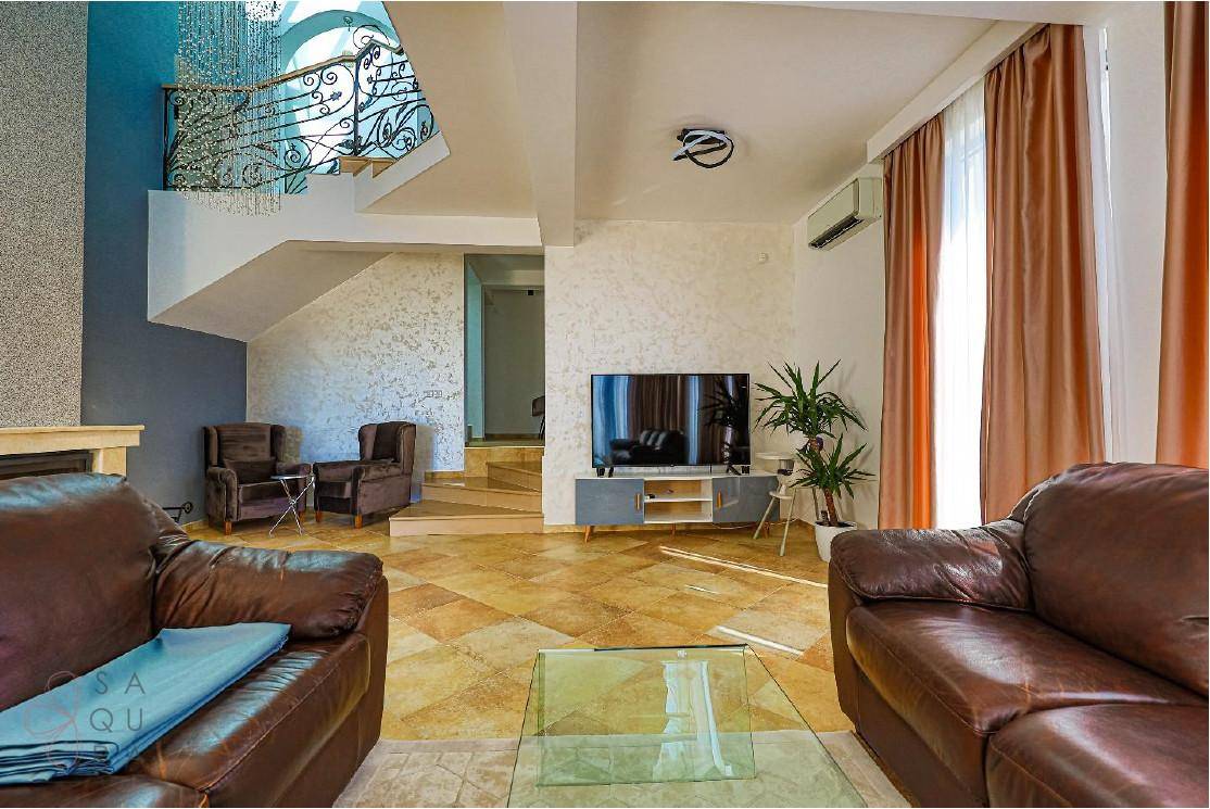 Helles Wohnzimmer mit Ledersofas, Fliesenboden und einem Fernseher, ergänzt durch eine Klimaanlage.