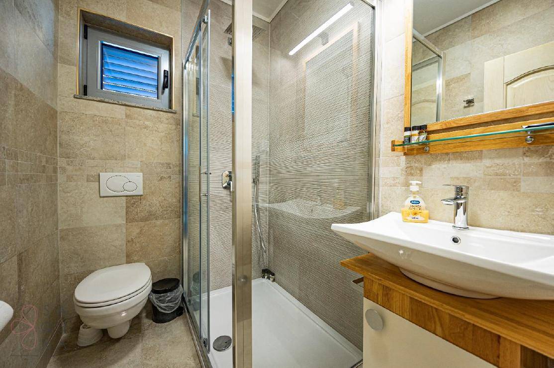 Modernes Badezimmer mit begehbarer Dusche, WC und Fenster, ausgestattet mit hellen Fliesen.