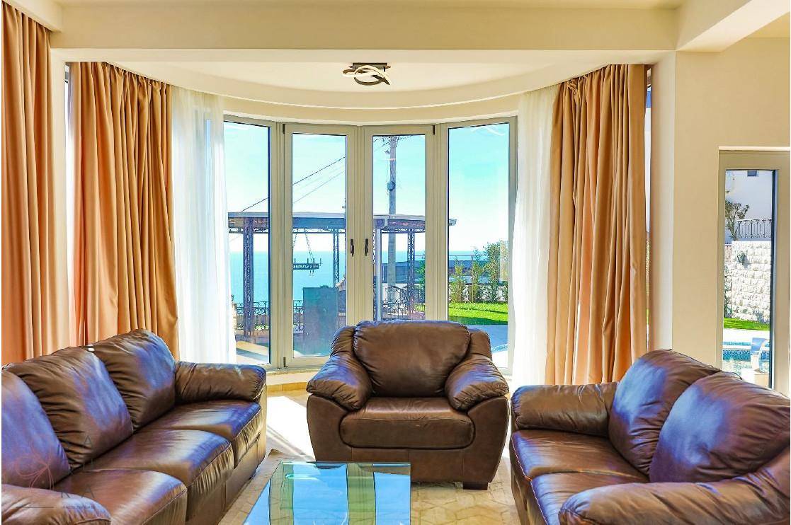 Helles Wohnzimmer mit bequemen Ledersofas und großen Fenstern, die einen Blick auf den Außenbereich und das Meer bieten.