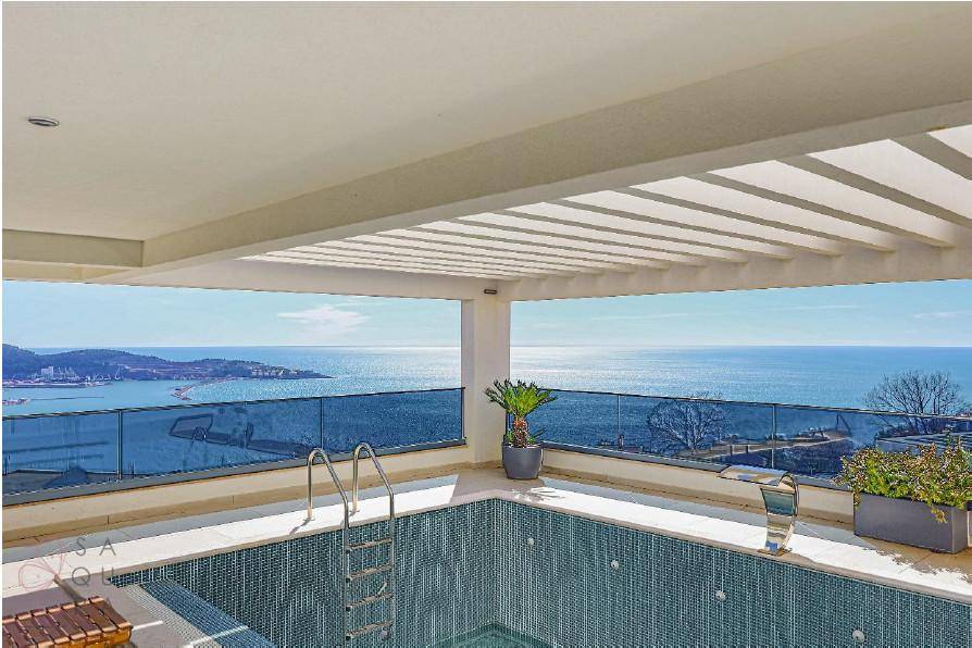 Panoramablick vom Poolbereich auf das Meer und die Küstenlandschaft unter blauem Himmel.