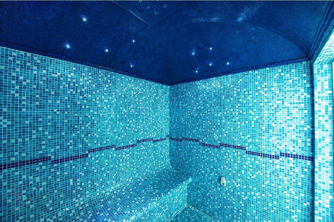 Detailansicht des Hamams mit blauen Mosaikfliesen und integrierten Sitzbänken unter einem Sternenhimmel.