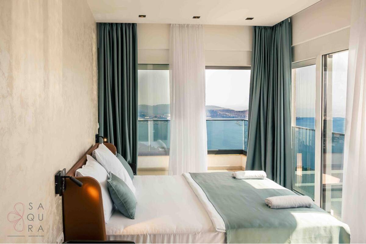 Schlafzimmer mit Meerblick, großen Fenstern und einem bequemen Bett mit blauen Akzenten.
