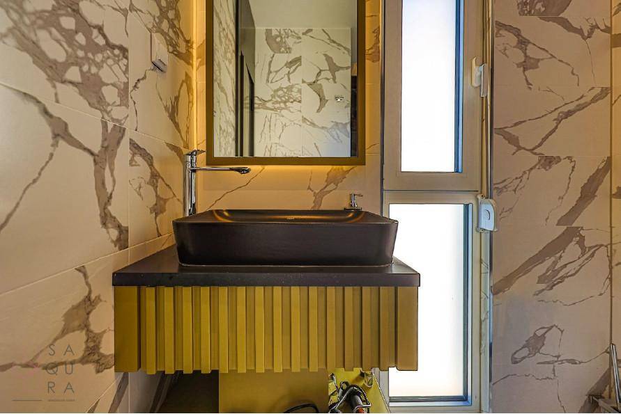 Modernes Badezimmer mit schwarzem Aufsatzwaschbecken, goldenem Unterschrank und Marmorwänden.