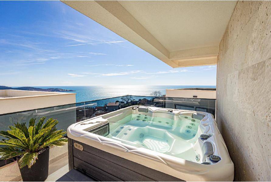 Luxuriöser Whirlpool auf einer Terrasse mit atemberaubendem Meerblick unter blauem Himmel.