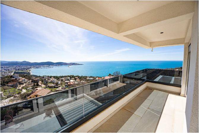 Weitläufige Terrasse mit Glasgeländer und Panoramablick auf das Meer und die Küstenstadt.