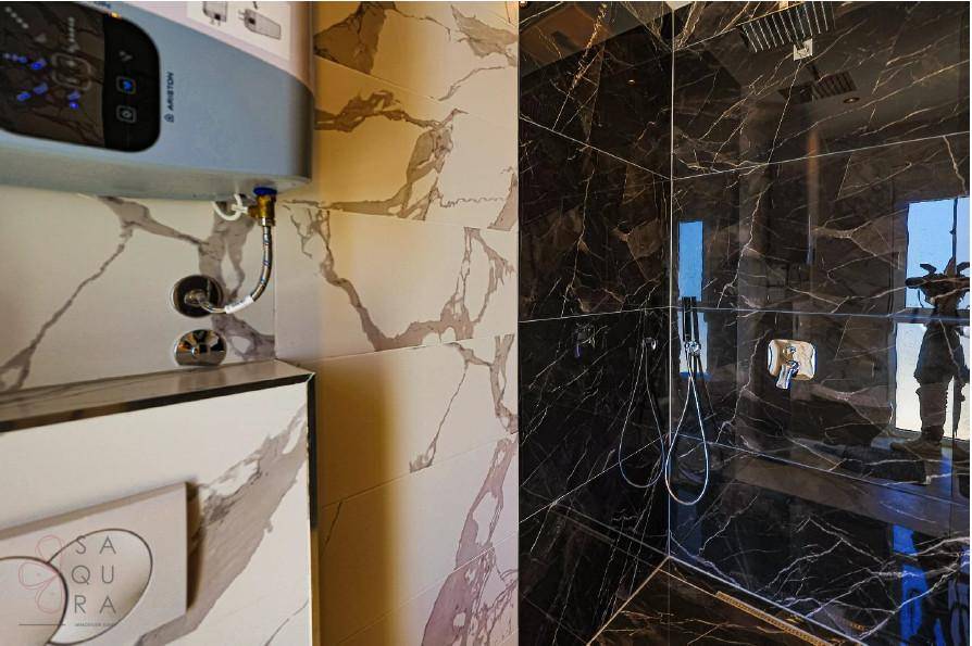 Badezimmerdetail mit modernem Warmwasserbereiter und luxuriöser Duschkabine aus dunklem Marmor.