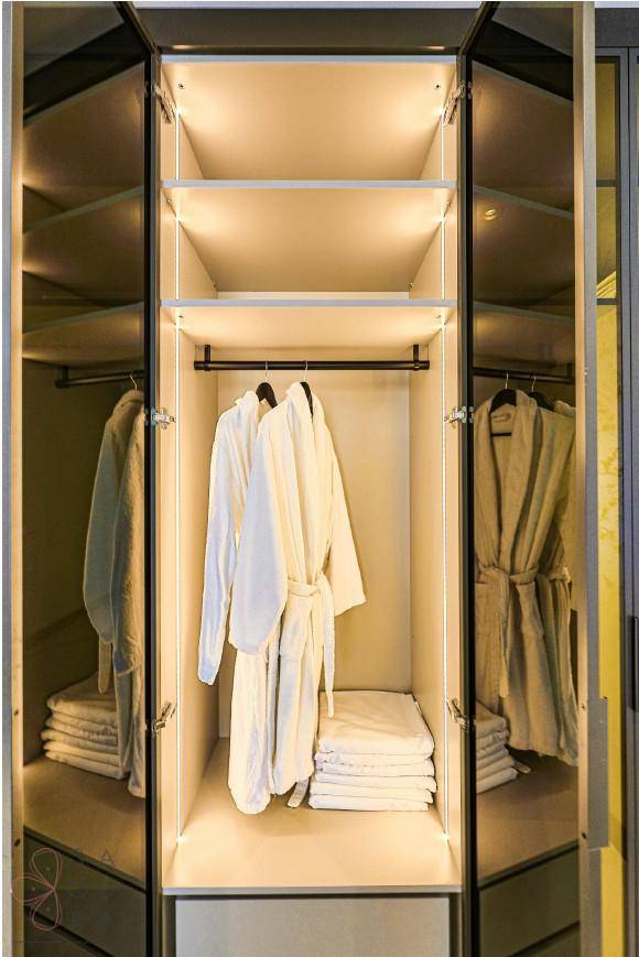 Beleuchteter Einbauschrank mit Bademänteln und gestapelten Handtüchern, ordentlich organisiert.