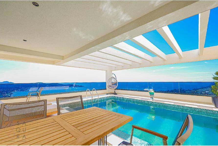 Geräumiger Außenbereich mit Pool, Essbereich und atemberaubendem Meerblick unter blauem Himmel.