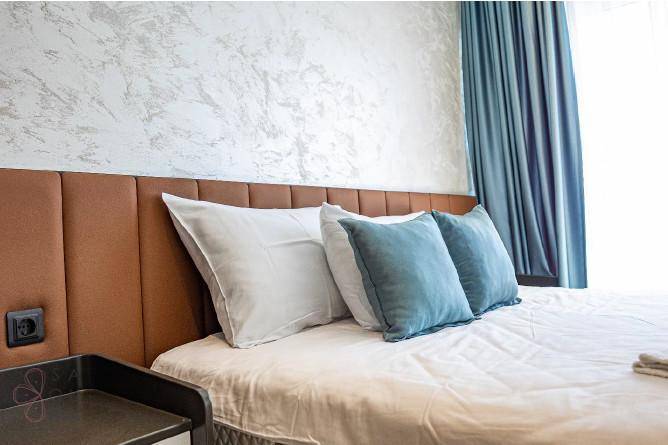 Detailansicht des Bettes im Schlafzimmer mit bequemen Kissen und einer strukturierten Wand.