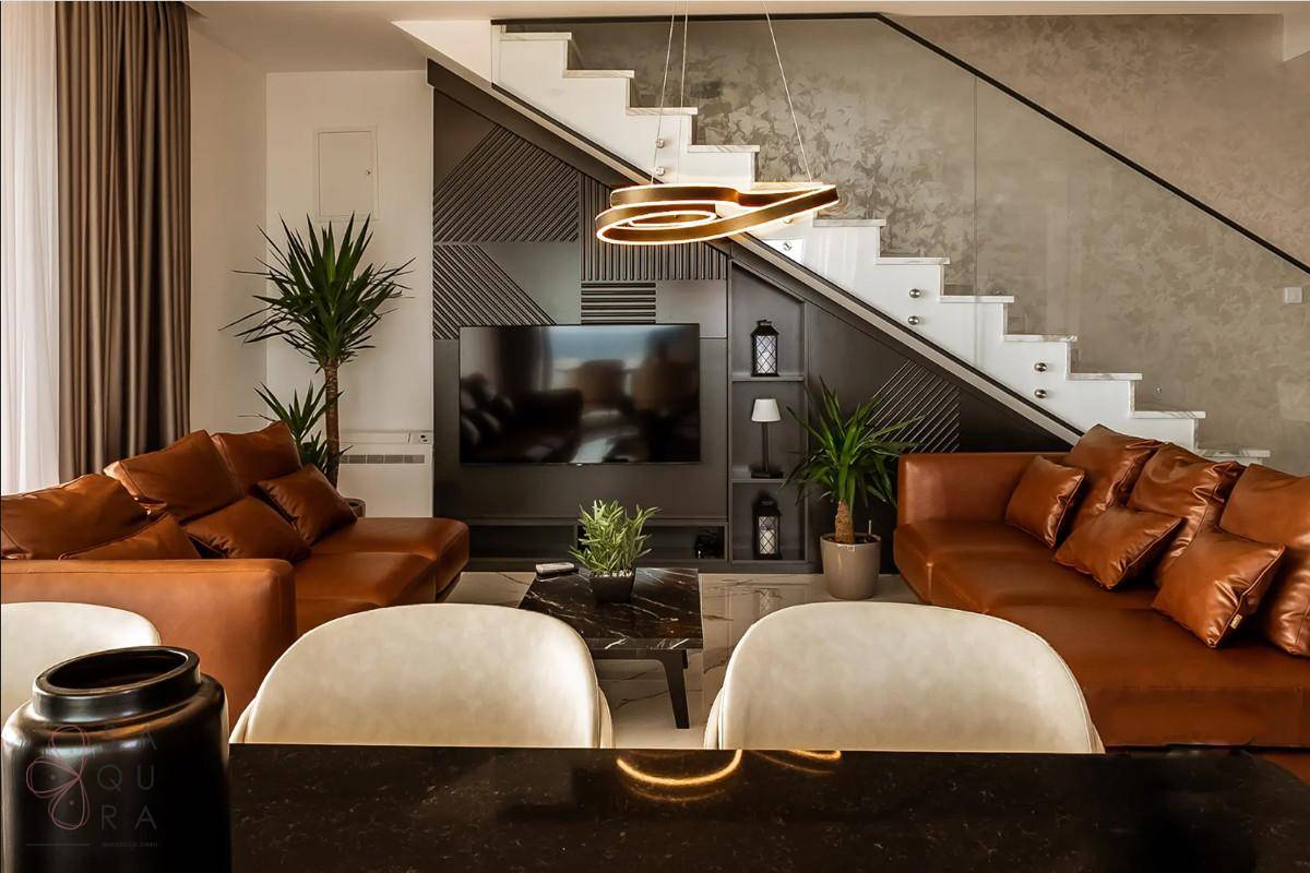 Gemütliches Wohnzimmer mit Ledersofas, Couchtisch und stilvoller Treppe im Hintergrund.