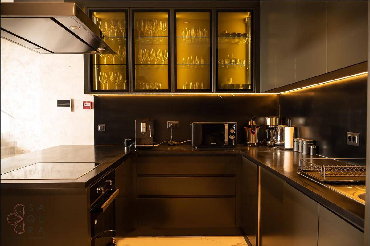 Dunkle, elegante Küche mit modernen Geräten, beleuchteten Glasvitrinen und viel Arbeitsfläche.