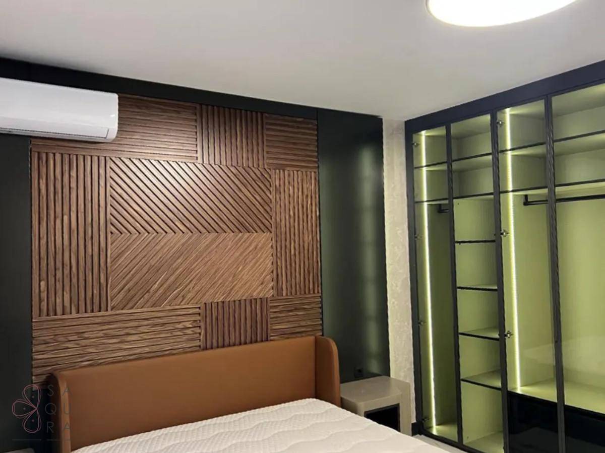 Schlafzimmer mit Holzwandverkleidung, modernem Bett und beleuchtetem Einbauschrank mit Glasfronten.