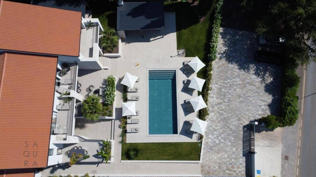 Draufsicht auf den eleganten Poolbereich mit Liegestühlen und Sonnenschirmen neben der Villa.