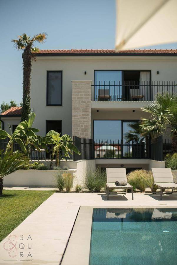 Gepflegter Gartenbereich mit Pool, Liegestühlen und mediterranen Pflanzen unter blauem Himmel.