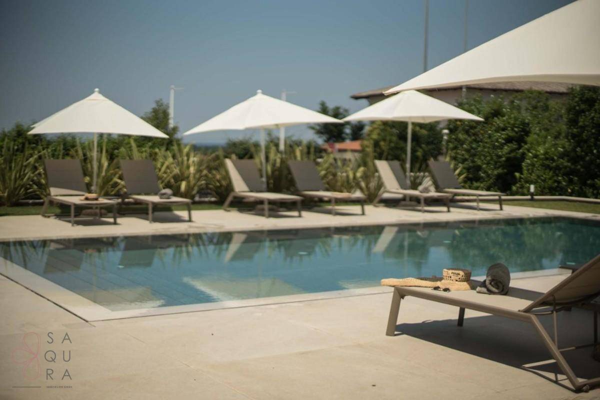 Großer Poolbereich mit mehreren Liegestühlen und Sonnenschirmen unter blauem Himmel.
