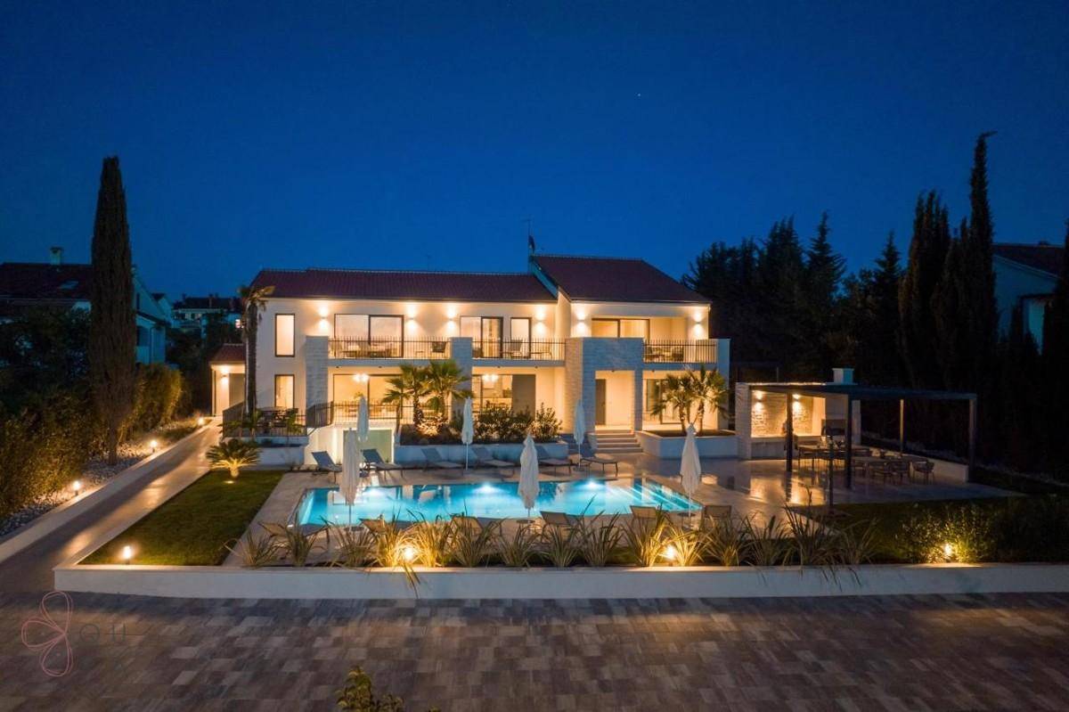 Beeindruckende Villa und Poolbereich bei Nacht, stimmungsvoll beleuchtet unter dunklem Himmel.